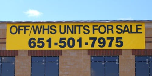 Yellow vinyl banner with black text promoting units for sale and listing a phone number.